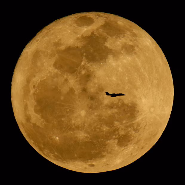 A small jet is silhouetted against the rising full moon in the skies above Phoenix, Arizona