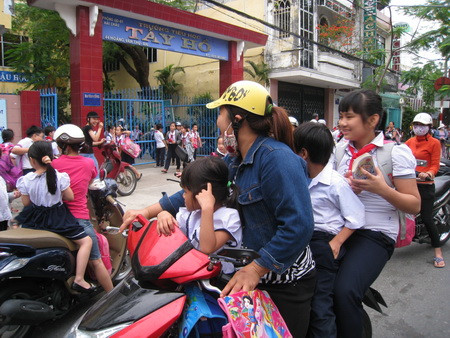 Nhiều trường hợp phụ huynh chở 2, chở 3 học sinh không đội mũ bảo biểm (ảnh chụp tại cổng Trường TH Tây Hồ, quận Hải Châu, Đà Nẵng)