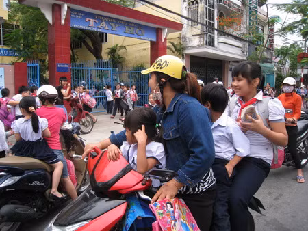 Nhiều trường hợp phụ huynh chở 2, chở 3 học sinh không đội mũ bảo biểm (ảnh chụp tại cổng Trường TH Tây Hồ, quận Hải Châu, Đà Nẵng)