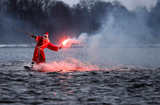 Sự kiện nổi bật của thế giới qua ảnh ảnh 7 A man dressed as Santa Claus holds a flare as he wakeboards at a water ski set on a lake in Hamburg