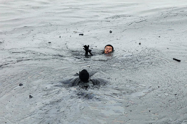 Những thảm họa thiên nhiên, một năm nhìn lại ảnh 20 A worker attempts to rescue his co-worker from drowning in the oil slick while attempting to fix an underwater pump during the oil spill clean-up operations at Dalian’s Port in Liaoning province, China