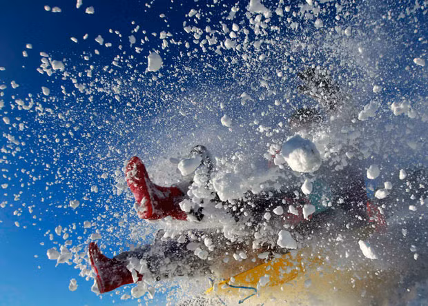 A sledger’s boots are visible in an explosion of snow during an attempt to jump a ramp at the Queen Elizabeth country park near Petersfield in Hampshire
