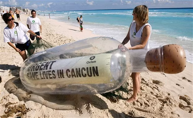 Oxfam activists carry a giant bottle on a beach in Cancun. The bottle contains a message reading 