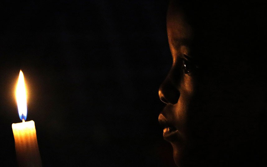 Một cậu bé đang cầm nến đứng bên ngoài nhà cố Tổng thống Nam Phi Nelson Mandela ở Johannesburg A South African boy holds a candle during a homage outside the Houghton home of the late former South African President Nelson Mandela in Johannesburg