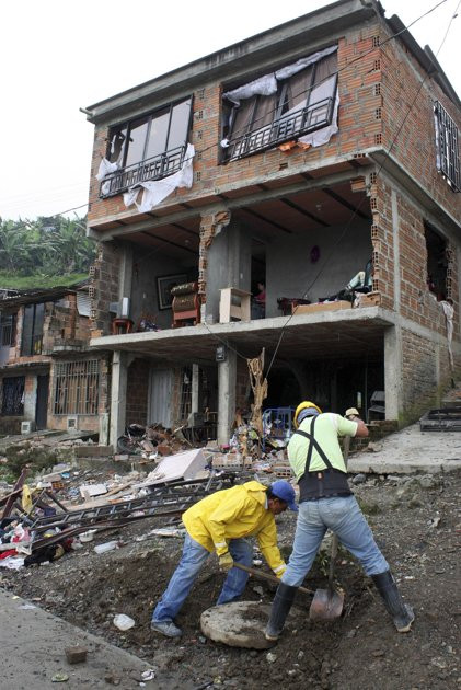 Men work in front of a home that was damaged by a pipeline explosion in Dos Quebradas, Colombia, Friday Dec.