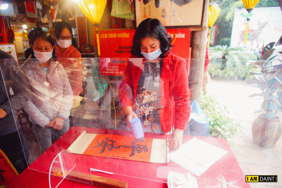 Ông đồ và sĩ tử đeo khẩu trang, đứng giãn cách khi cho chữ, xin chữ, kính chắn giọt bắn được đặt trên bàn cho chữ để phòng Covid-19.