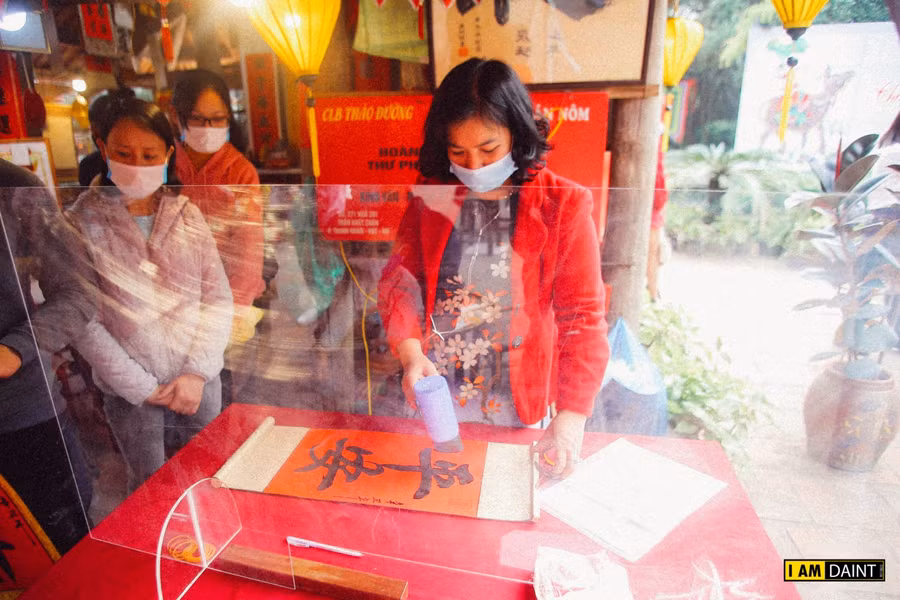 Ông đồ và sĩ tử đeo khẩu trang, đứng giãn cách khi cho chữ, xin chữ, kính chắn giọt bắn được đặt trên bàn cho chữ để phòng Covid-19.