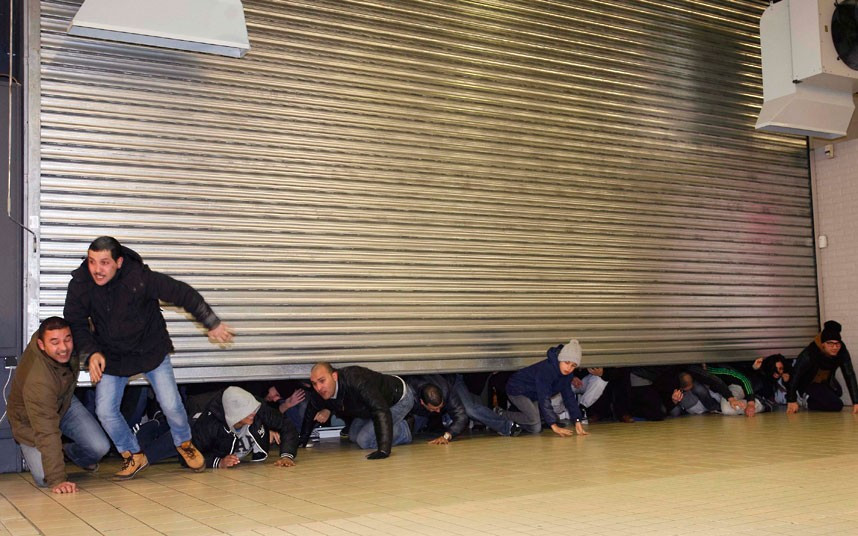 Những hình ảnh ấn tượng trong tuần ảnh 12 Shoppers crawl under a metal shutter as it slowly rolls up at Cora general store, in Mons, northern France, on the first day of the winter sales