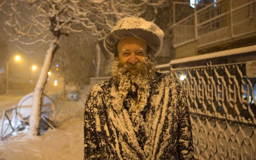 An Ultra-Orthodox Jewish man walks through a snowstorm in Jerusalem