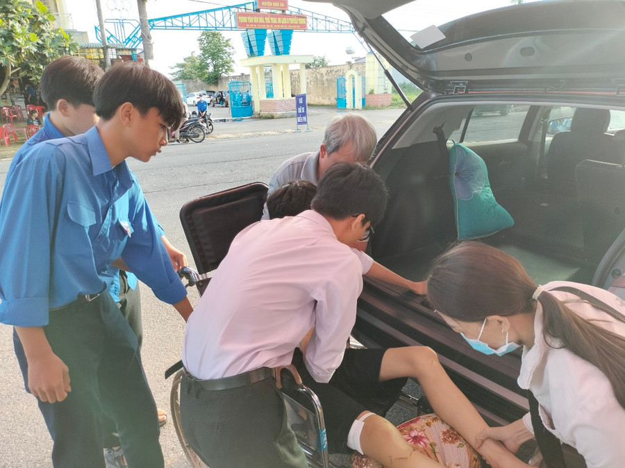 Tình nguyện viên cùng gia đình đưa thí sinh Thái từ xe ô tô xuống xe lăn an toàn.