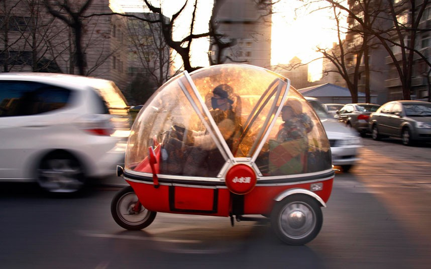 Những hình ảnh ấn tượng trong tuần ảnh 7 A woman and her son sit inside the capsule of an electric tricycle as they drive along a main road in central Beijing