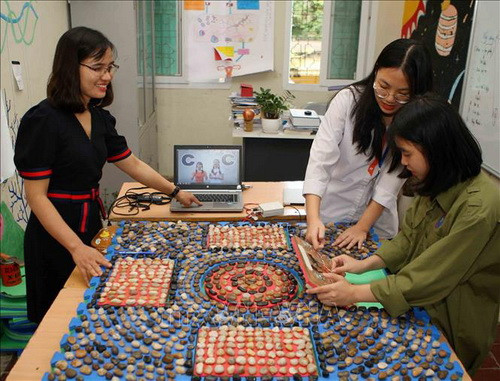 Cô giáo Dương Thị Thu Hà cùng các em học sinh thực hiện dự án hỗ trợ trẻ mắc bệnh Down học chữ cái thông qua các chủ đề kỹ năng sống với thiết bị PSE (Pictures, Sounds, Expressions) do cô cùng học sinh tự nghiên cứu, thiết kế và chế tạo. Ảnh: Thanh Tùng/TTXVN
