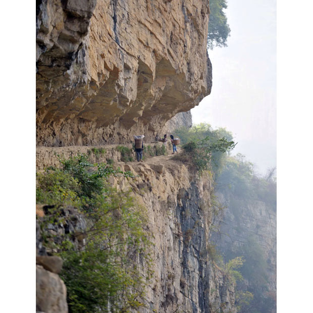 8-year-old Yang Wei (flowery dress) and other children make a journey along a mountain path to fetch water in Chahe village, Sichuan Province, China. Southwest China is currently experiencing the worst drought in 50 years, affecting some 17 million people. Xu Yong County in Sichuan Province is one of the worst affected places. Chahe village is at a high altitude in the mountains and this year there is a severe lack of drinking water as the streams that are the village’s main water supply have dried up. 8-year-old Yang Wei lives in Chahe village with her grandmother and little brother while her parents work in another city. Each day Yang has to make numerous trips to several local caves in order to collect water for their daily needs. The cave where the water is located is in the middle of a vertical cliff 1km away from the village. There’s no proper road along the cliff to the cave, only some narrow walkways that have been chipped out from the stone. At its widest, this walkway measures 1 meter across but at its slimmest there is only half a foot.