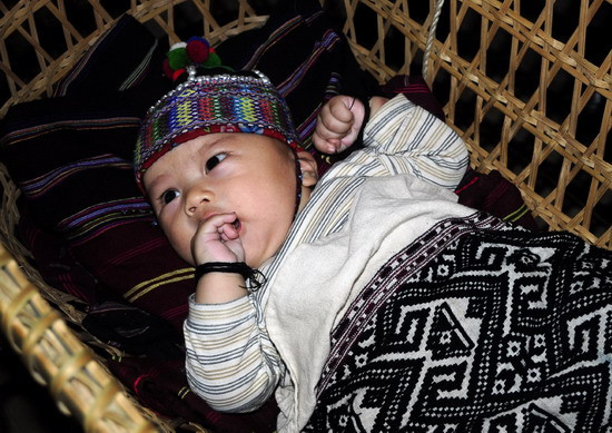 em bé xinh xắn đáng yêu nằm trong nôi với chăn đệm thổ cẩm của dân tộc mình