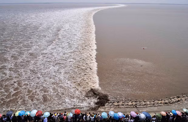 A remote controlled helicopter hovers over the Qiantang River as tourists gather on the river bank to see the tidal bore in Haining, Zhejiang province. China
