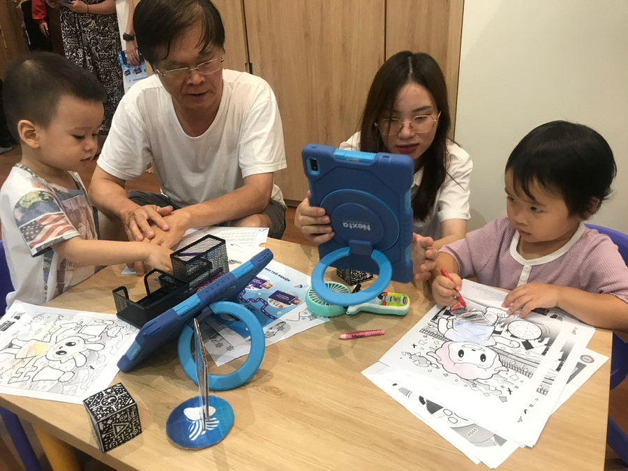 Cô giáo hướng dẫn cả ông và cháu sử dụng ứng dụng qua máy tính bảng.