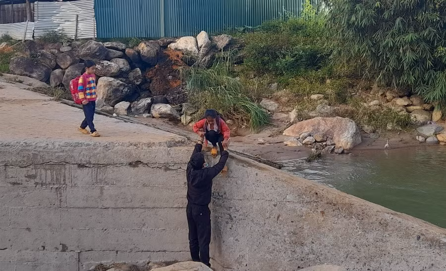 Mố cầu bị nước lũ cuốn trôi, giáo viên túc trực để bế trò vượt suối đến trường.