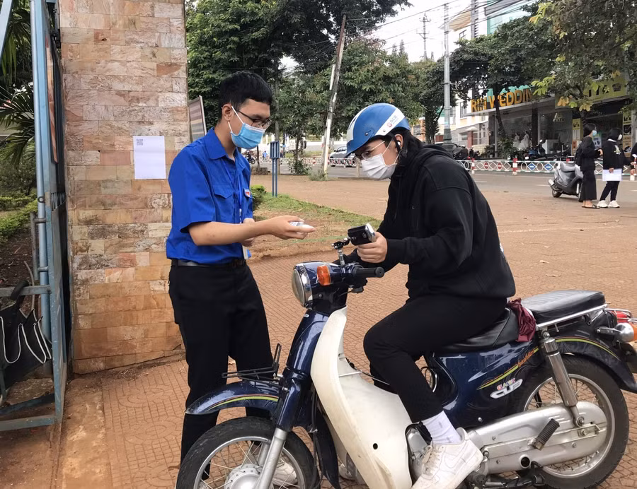 Tình nguyện viên hỗ trợ đo thân nhiệt, sát khuẩn trước khi thí sinh vào điểm thi.