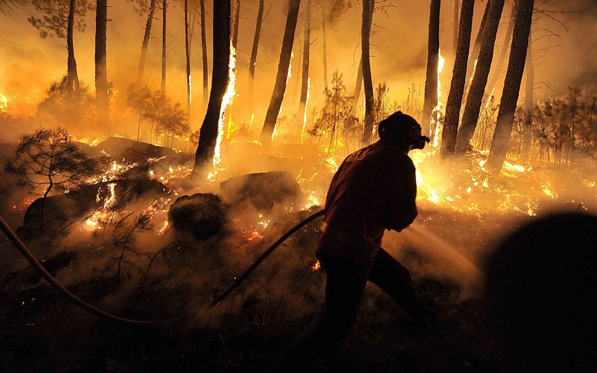 A fireman is silhouetted against the flames as teams of firefighters from across the country try to stop the forest fire at Moimenta da Beira, Portugal.