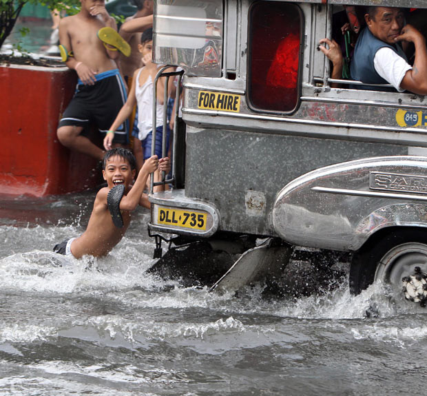 A boy clings onto a passenger jeep on a flooded street in Manila, Philippines