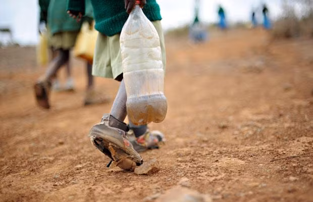 A boy carries a plastic bottle filled with river water as he and others head back to school on August 17, 2009. Regularly recurring droughts in Kenya are forcing huge numbers of rural farmers into congested slums