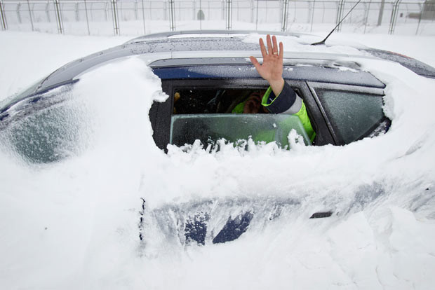 Những hình ảnh ấn tượng trong tuần ảnh 5 A man waves from a car stranded in the snow on the outskirts of Bucharest, Romania. The man, who declined to be identified, spent the night in the car fearing it would be damaged by road clearing vehicles if he abandoned it.