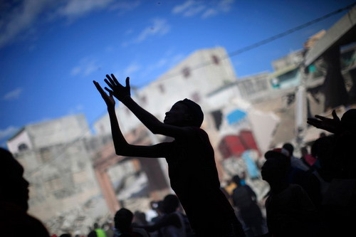 A woman raises her arms for products as people loot from a destroyed shop after Tuesday’s earthquake in Port-au-Prince