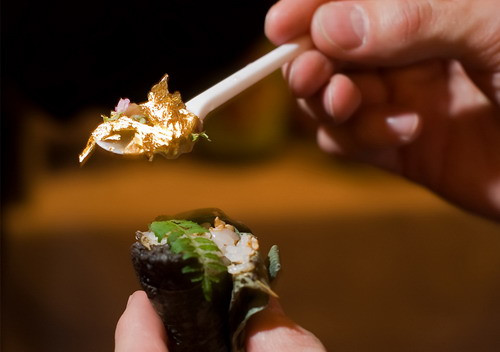 A man holds a spoon full of gold leaf, ready to eat it with his sushi at the 