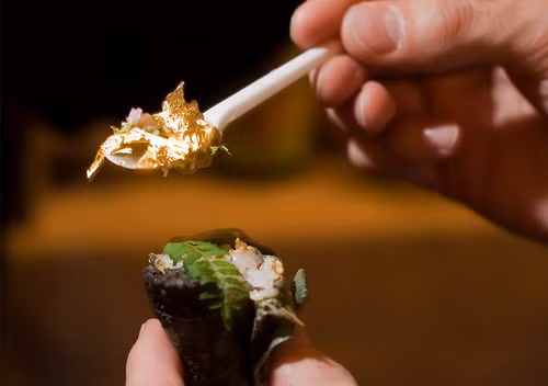 A man holds a spoon full of gold leaf, ready to eat it with his sushi at the 