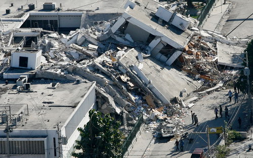 Haitians survey the damage to a building that collapsed onto a road in downtown Port-au-Prince