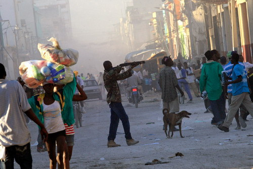 A man points a gun toward a crowd in downtown Port-au-Prince January 15, 2010. The man fired warning shots into the air to prevent looters from ransacking his shop, a Reuters photographer witnessed