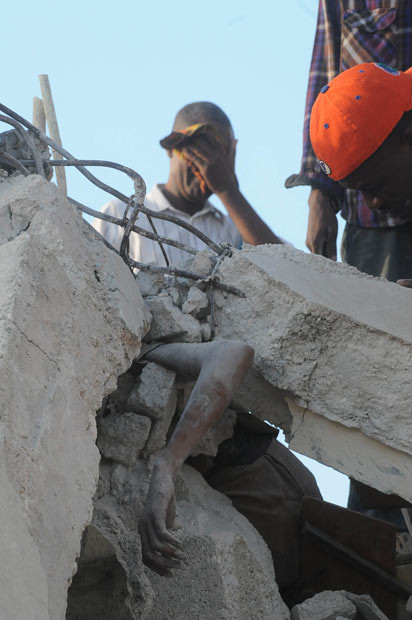 Kinh hoàng khi tìm kiếm nạn nhân trong đống đổ nát ở Port-au-Prince A man covers his face behind a person trapped in the rubble of a collapsed building in Port-au-Prince