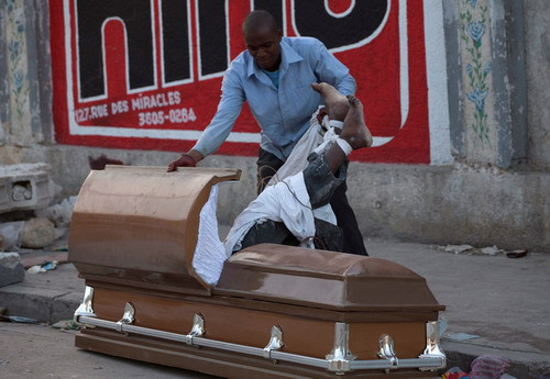 A man pulls the body of an earthquake victim from a coffin in order to steal the coffin at the cemetery in Port-au-Prince,