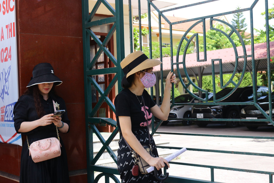 Khuôn mặt hằn rõ mệt mỏi, những người mẹ đưa ánh mắt hướng vào trong điểm thi ngay cả khi cổng trường đang khóa chặt.