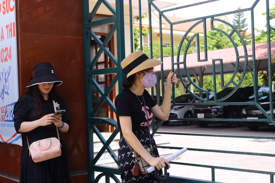 Khuôn mặt hằn rõ mệt mỏi, những người mẹ đưa ánh mắt hướng vào trong điểm thi ngay cả khi cổng trường đang khóa chặt.