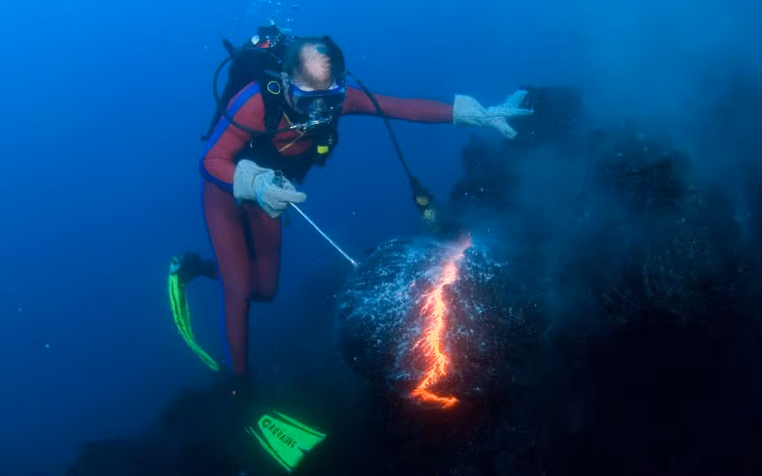 Diver Bud Turpin shapes erupting pillow lava into a sculpture of a moose head during an underwater eruption of Kilauea Volcano, Hawaii