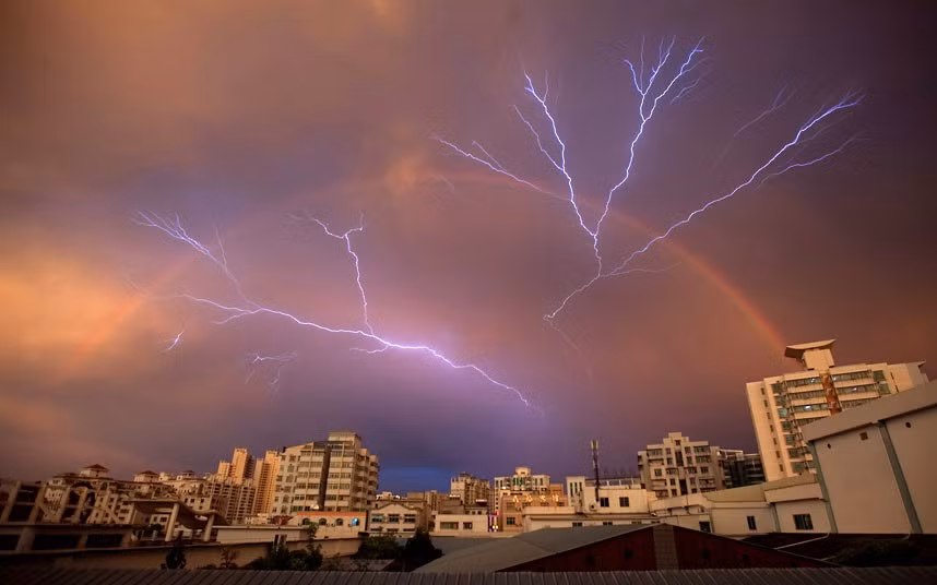 A rainbow is seen in the sky as lightning strikes after a rainstorm in Haikou, Hainan province, China