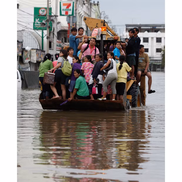 Residents ride on a digger as it makes its way down a flooded road in Nakhon Ratchasima province, Thailand