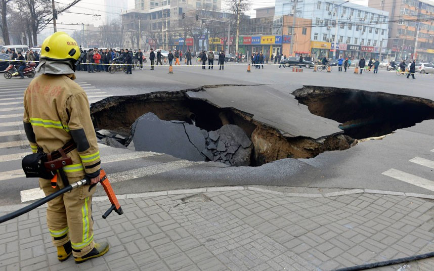 Những hình ảnh ấn tượng trong tuần ảnh 8 A firefighter stands next to a caved-in road at an intersection in Taiyuan, Shanxi province, China. The cause of the cave-in, measuring about six metres in depth and 10 metres in diameter, is still under investigation. Three coal gas pipes and one water main were ruptured during the collapse.