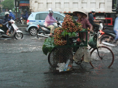 Mưa ập xuống nhanh đến nỗi bác bán quà rong này không kịp mặc áo mưa, chỉ còn biết đội mưa, cười tươi khi thấy ống kính máy ảnh hướng đến. Ảnh, gdtd.vn