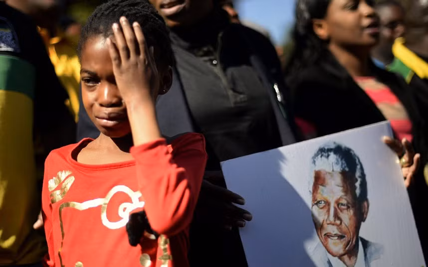 A girl weeps as she stands next to a portrait of Nelson Mandela held by ANC supporters outside the Medi-Clinic Heart Hospital, where the ailing former South African President is being treated, in Pretoria