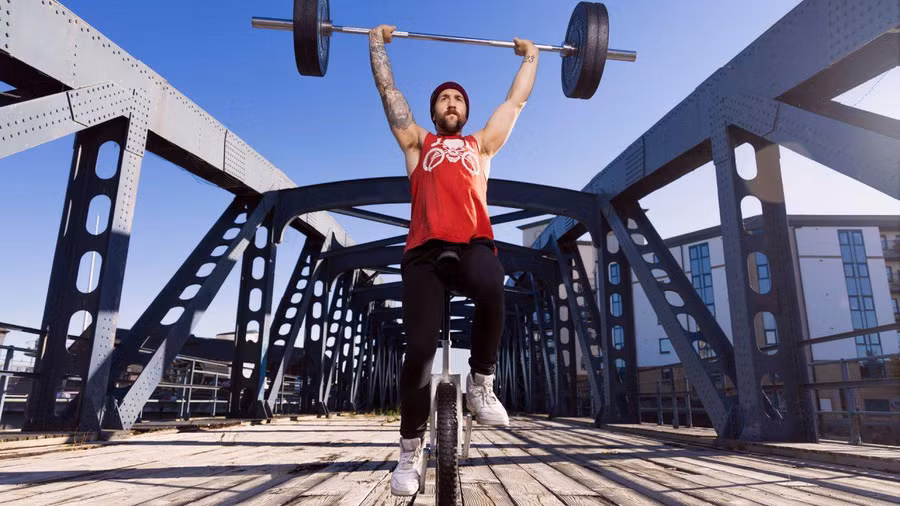 Josh Auld, đến từ Edinburgh (Scotland) đã giành được Kỷ lục Guinness về việc nâng một quả tạ nặng 68 kg qua đầu khi đi xe đạp một bánh. Ảnh: Guinness World Records.