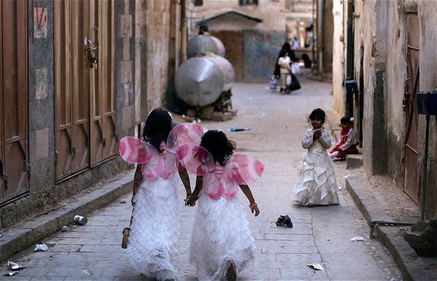 Two sisters dressed as angels hold hands while walking in an alley of the old city, in Sanaa, Yemen