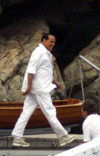 Thủ tướng Italia Silvio Berlusconi chuẩn bị lên du thuyền ở Sardinia. Grinning like a Cheshire cat, Silvio Berlusconi prepares to board the yacht of Formula One mogul Flavio Briatore in Sardinia.