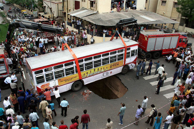 Kinh hoàng những hố địa ngục trên thế giới ảnh 5 July 2010: People watch as rescue workers and fire service personnel use cranes to lift a bus after a road underneath it caved in, in Ahmedabad, India