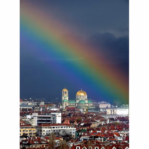 The golden dome of the Alexander Nevski Cathedral glows as a rainbow forms over Sofia, Bulgaria