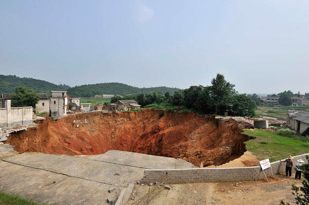 Kinh hoàng những hố địa ngục trên thế giới ảnh 7 June 2010: Local residents look at a sinkhole near Qingquan primary school in Dachegnqiao town, Ningxiang, Hunan province, China. The hole, 150 metres (492 feet) wide and 50 metres (164 feet) deep, has been growing since it first appeared in January and has destroyed 20 houses so far