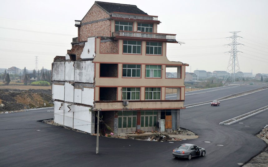 A car drives around a house that stands in the middle of a newly-built road in Wenling, Zhejiang province, China. An elderly couple refused to sign an agreement to allow their house to be demolished. They say that the compensation offered was not enough to cover rebuilding costs. Their house is the only building left standing on a road which is paved through their former village. 