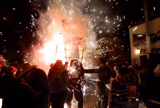 A reveller, carrying a bull’s head made cardboard, takes part in carnival celebrations amidst exploding fireworks as people get out of his way in Zapotitlan, outskirts of Mexico City