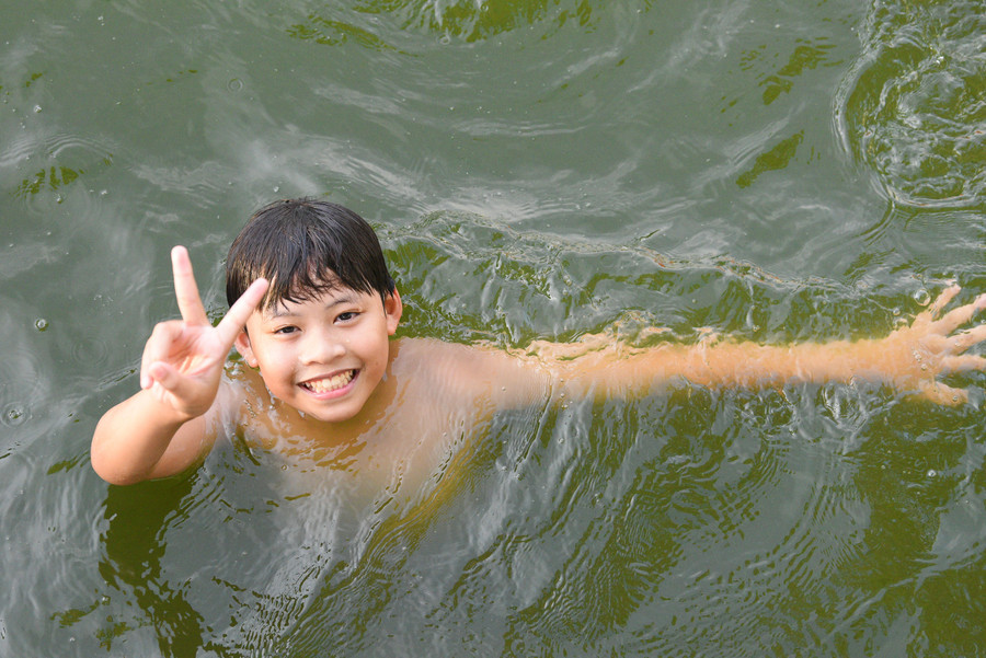 Người dân ngồi trên bờ cũng chăm chú quan sát con, em mình tắm dưới ao.